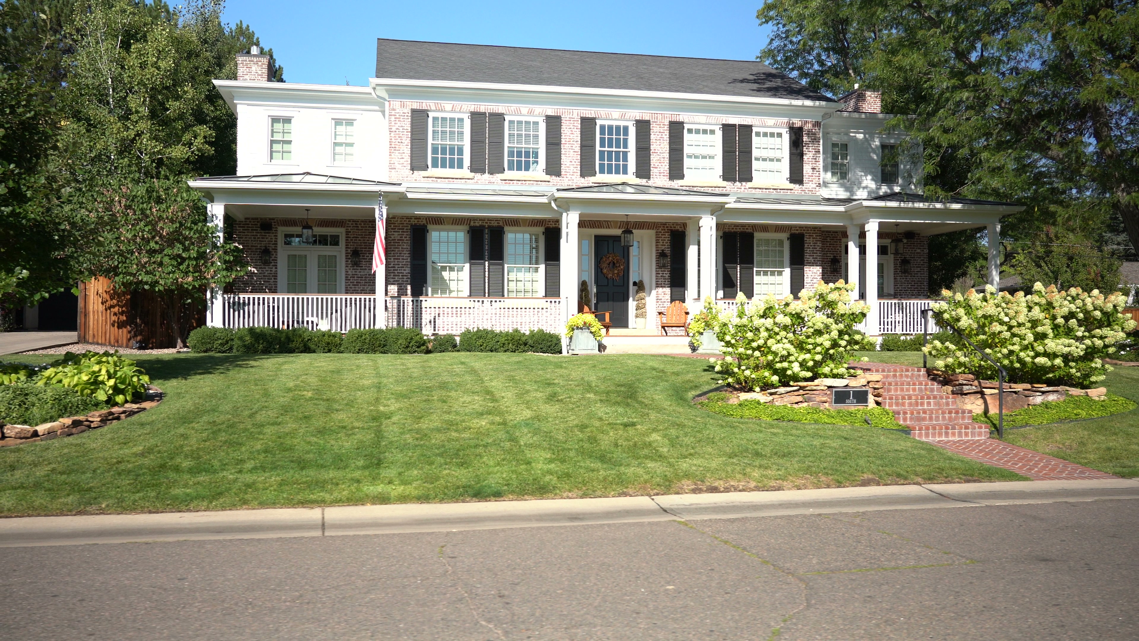 Large two-story brick Colonial home in Denver Hilltop with white columned porch, hydrangeas, and manicured front lawn