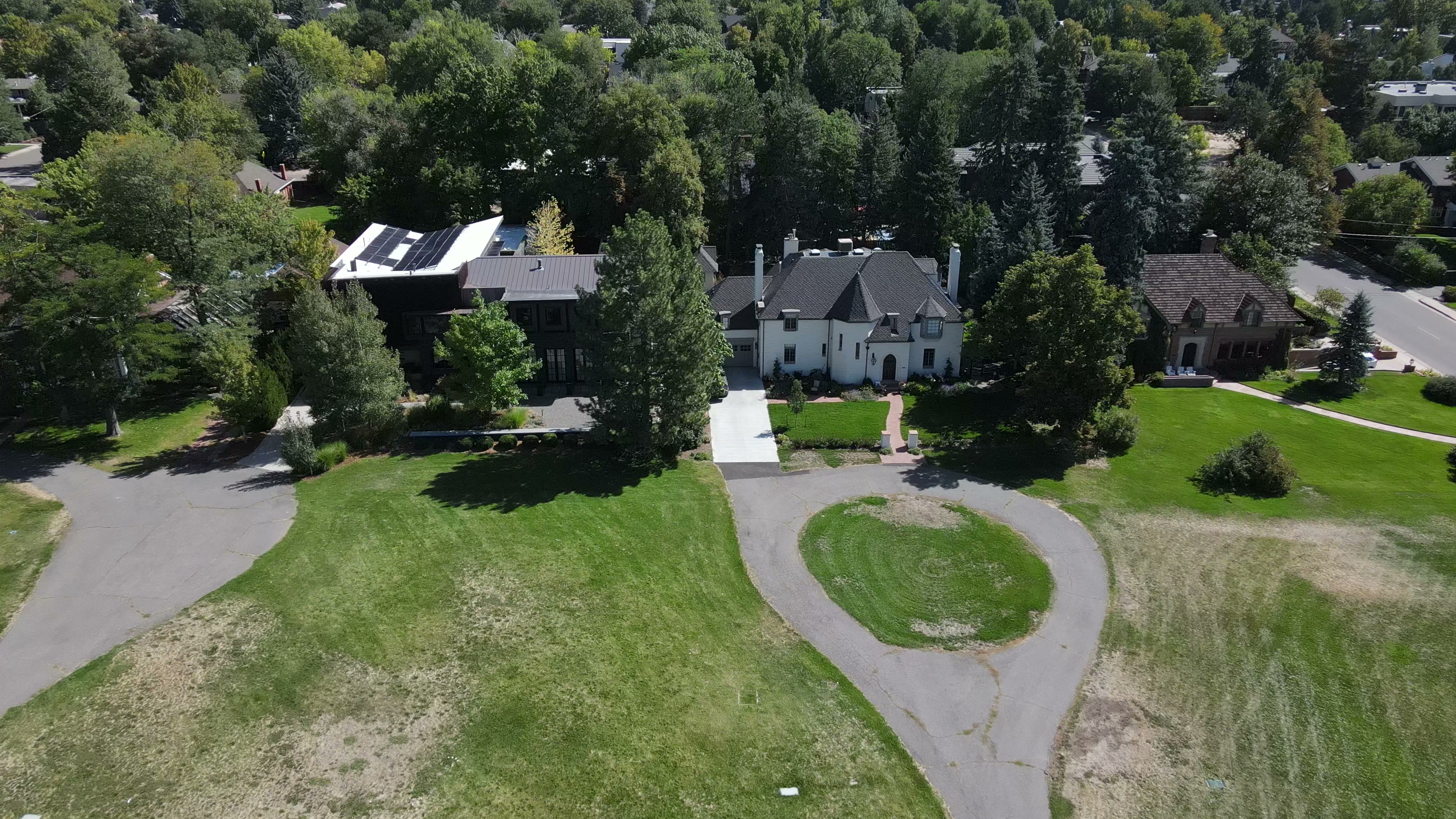 Aerial drone view of Denver Hilltop luxury estate homes with circular driveways, solar panels, and mature tree canopy bordering open green space